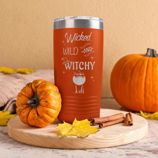 Custom Orange Tumbler With Wicked Wild And Witchy Text And Cauldron Art And Name Standing On Cutting Board Beside Pumpkins