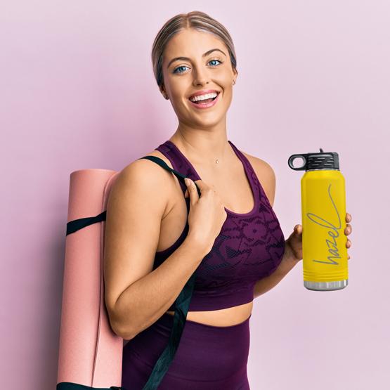 Custom Engraved 32 oz Yellow Water Bottle held by a happy woman with a sample engraving for Hazel