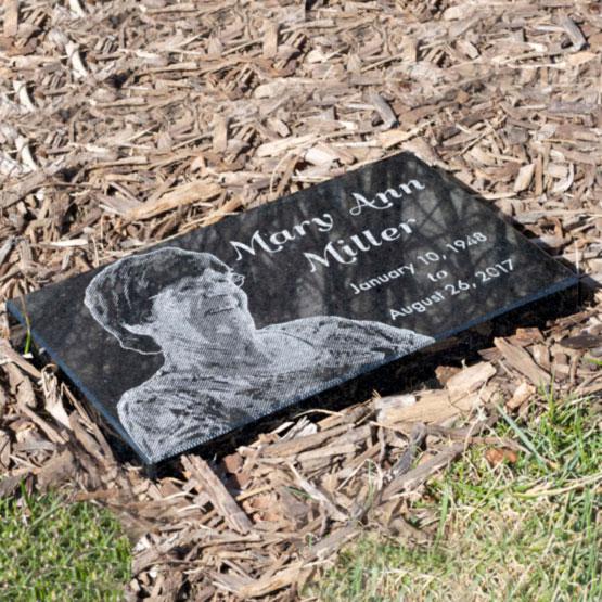 Custom Engraved Granite Headstone for Mary Ann Miller with her picture engraved into the stone. This headstone is placed among mulch.