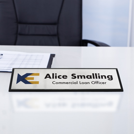 Custom Black Piano Desk Wedge Name Plate with Silver Metal Plate with Name and Logo on desk near papers.